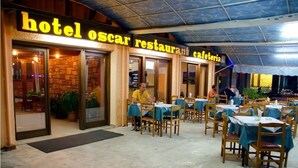 A restaurant with outdoor seating, tables covered with blue tablecloths, and a sign reading "hotel oscar restaurant cafeteria". - Oscar Hotel (Igoumenitsa)