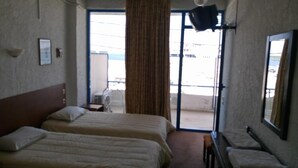 A hotel room with two beds, a small table, a chair, a large window with curtains, and a view of the outside. - Oscar Hotel (Igoumenitsa)