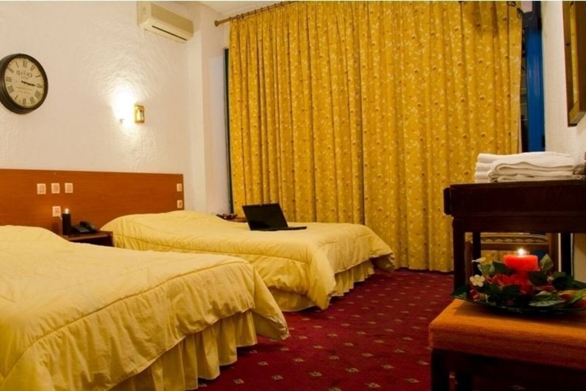 A hotel room with two beds, a clock on the wall, a desk with a laptop, and a curtain.