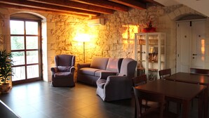 A cozy living room with a stone wall, a sofa, a chair, a table, and a cabinet. - Tenuta Zannafondo (Ragusa)