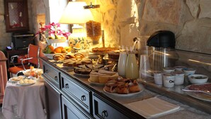 A buffet with various food items, including pastries, fruits, and beverages, set against a stone wall backdrop. - Tenuta Zannafondo (Ragusa)