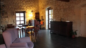 A rustic stone-walled room with a dining area, a sofa, and a kitchen area with cabinets and a sink. - Tenuta Zannafondo (Ragusa)
