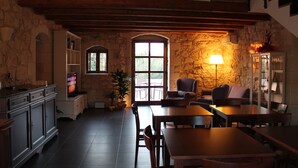 A cozy dining area with wooden tables and chairs, a stone wall, and a large window providing natural light. - Tenuta Zannafondo (Ragusa)