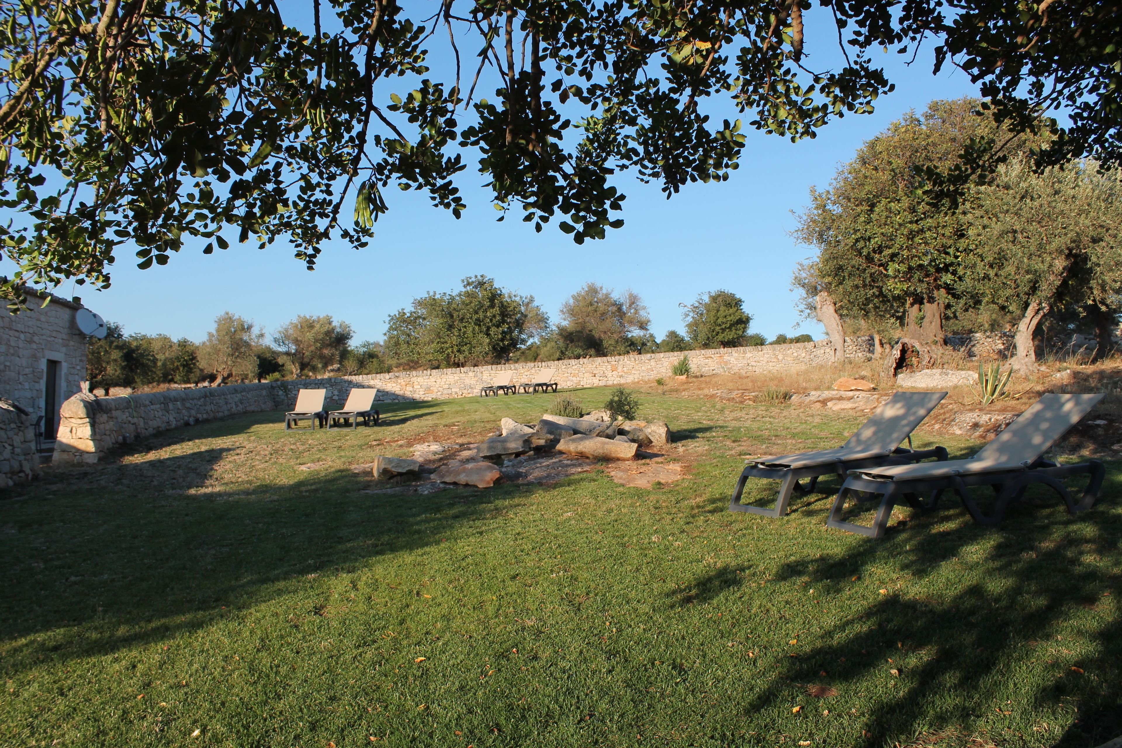 A stone wall with lounge chairs and a small table in a grassy area.