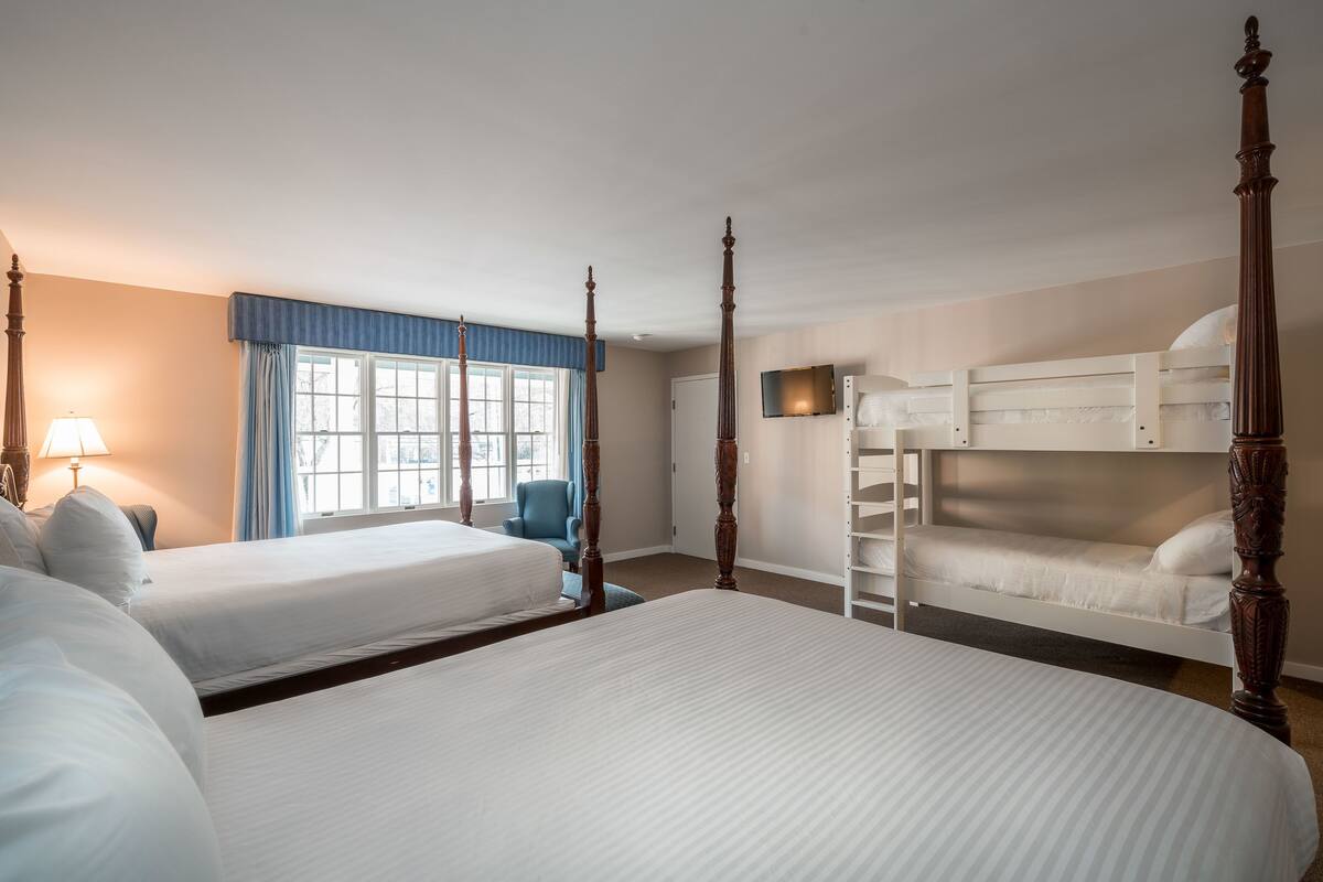 Habitación de hotel con dos camas tamaño queen, una litera, un escritorio y una silla.