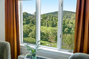 A room with a large window offering a view of a green landscape with trees and hills.