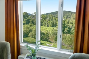 A room with a large window offering a view of a green landscape with trees and hills. - The Shire Woodstock (Woodstock)