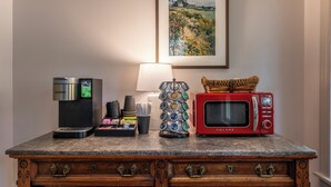 Una kitchenette con una cafetera Keurig, un microondas Balanz rojo, una estación de café y un cuadro enmarcado con un paisaje.