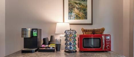 A kitchenette with a coffee maker, a microwave, and a coffee station with cups and a basket.