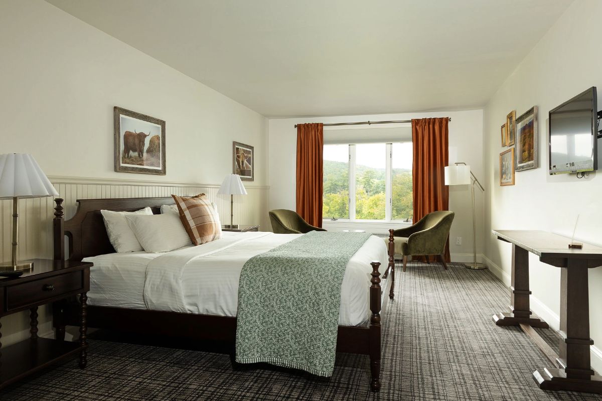 A hotel room with a bed, two chairs, a desk, and a window with curtains.