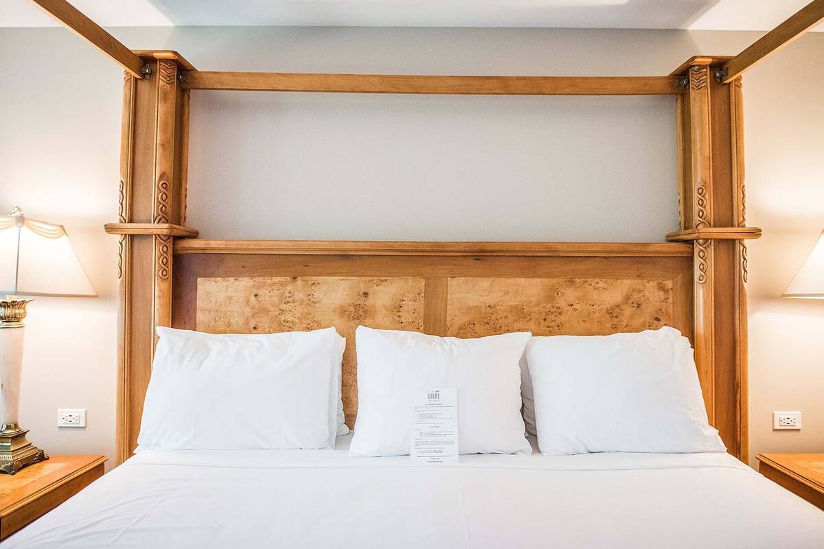 Habitación de hotel con cabecera de madera, ropa de cama blanca y dos lámparas de noche.