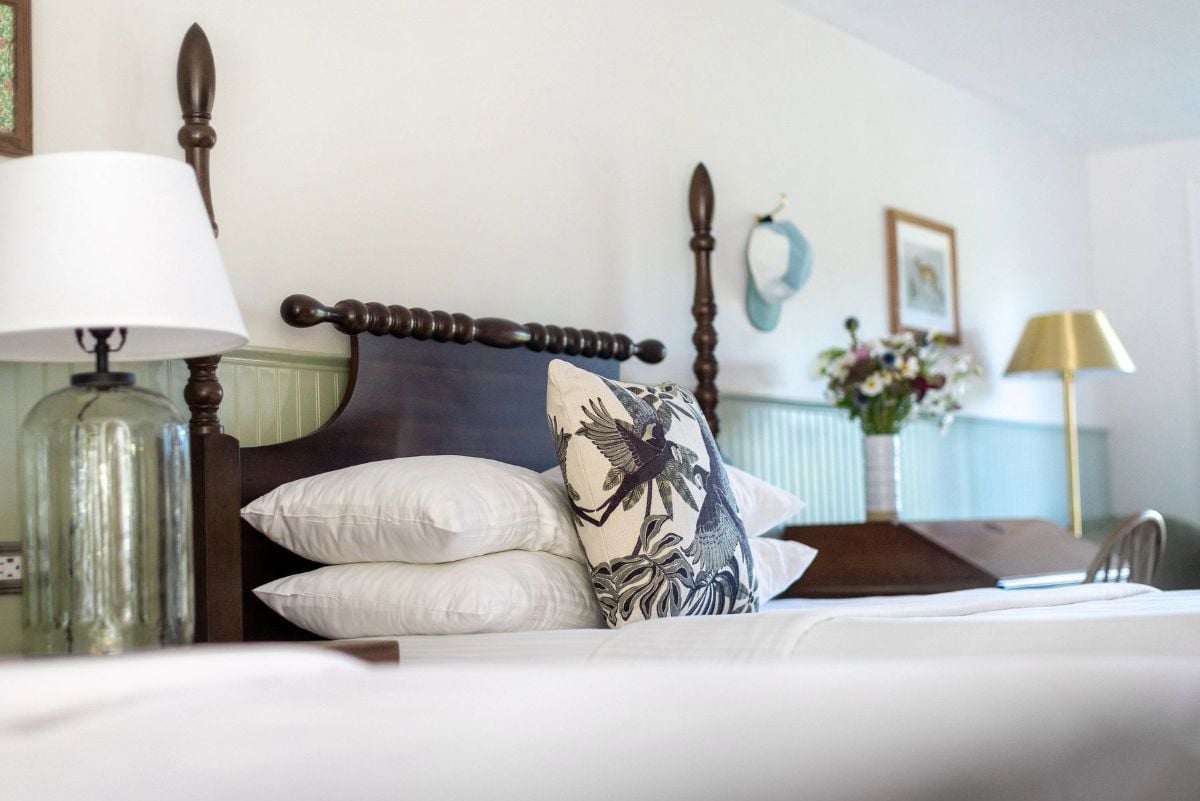 A neatly made bed with white linens and decorative pillows, a wooden headboard, and a bedside table with a lamp.