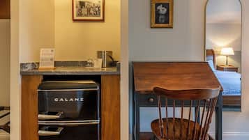 A hotel room with a black Galanz refrigerator, a wooden chair, a small table, a bed, and a wall-mounted mirror.