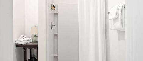 A bathroom with a shower, a towel rack, and a table with towels.