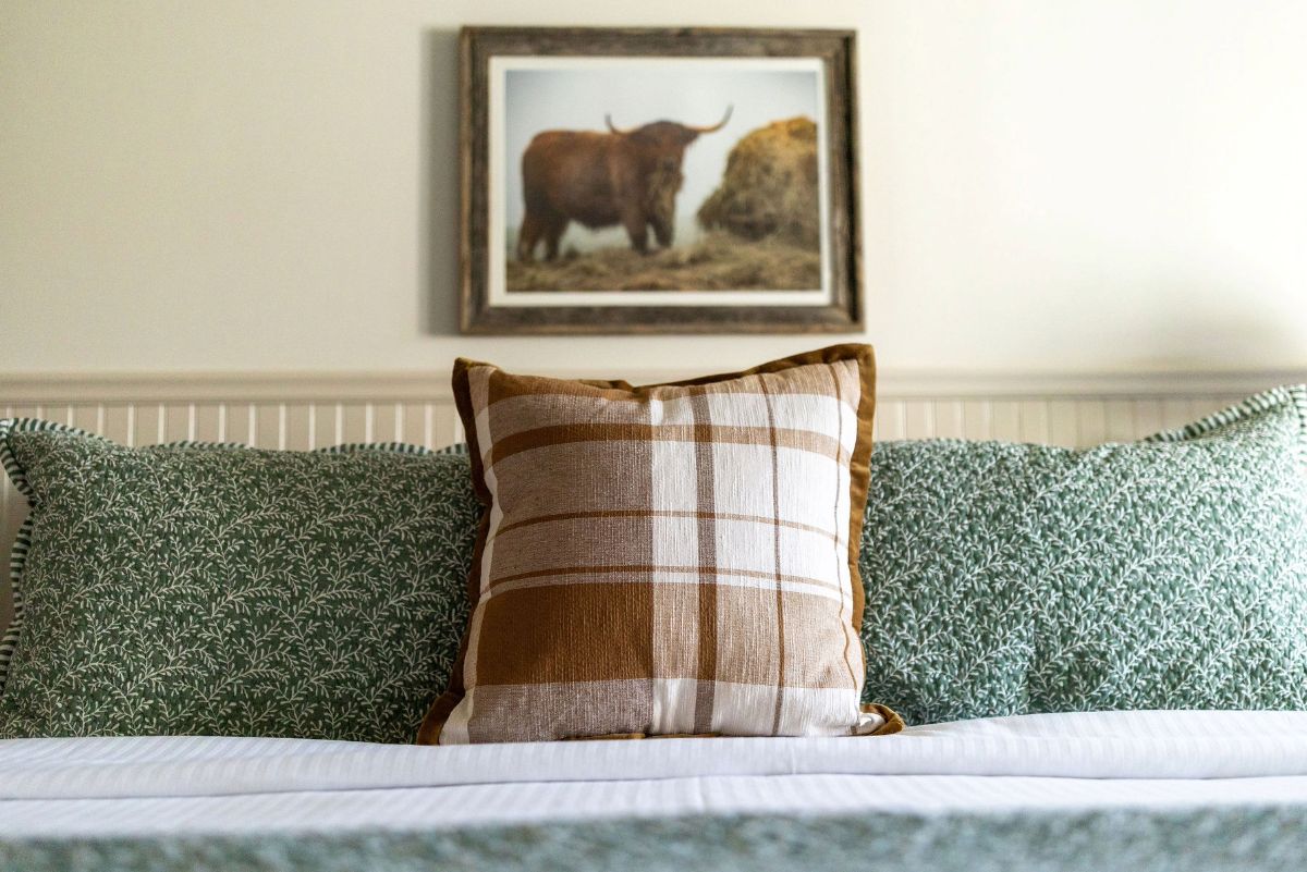 A bed with a striped pillow and green patterned pillows, a framed picture on the wall, and a white headboard.