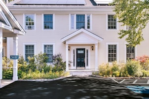 A two-story building with a central entrance, a small porch, and a driveway leading to a parking area.