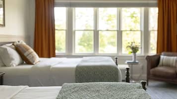 Quarto com duas camas, janela com cortinas, uma mesinha com um vaso e uma cadeira.