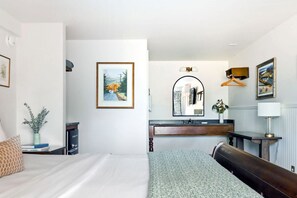 Una habitación de hotel con cama, mesita de noche, lámpara, cómoda, espejo y cuadros en las paredes.