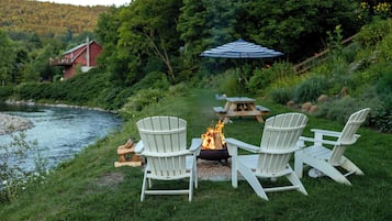 Un espacio al aire libre junto al lago con sillas Adirondack y un brasero.