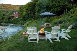 Een terras aan het meer met Adirondack-stoelen en een vuurkorf.