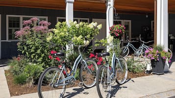 A building with a porch, two bicycles parked in front, and a variety of flowering plants.