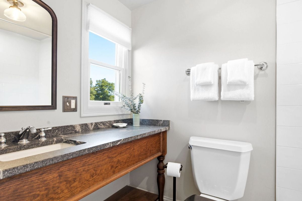 Un baño con encimera de mármol, tocador de madera, inodoro blanco y un espejo grande.