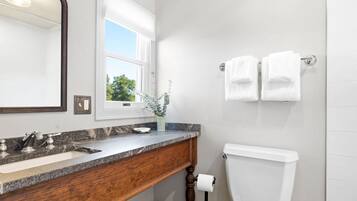Un baño con encimera de mármol, tocador de madera, inodoro blanco y un espejo grande.