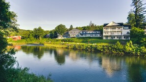 Vista de un lago con un edificio de varios pisos y balcones, rodeado de abundante vegetación y un lago tranquilo.