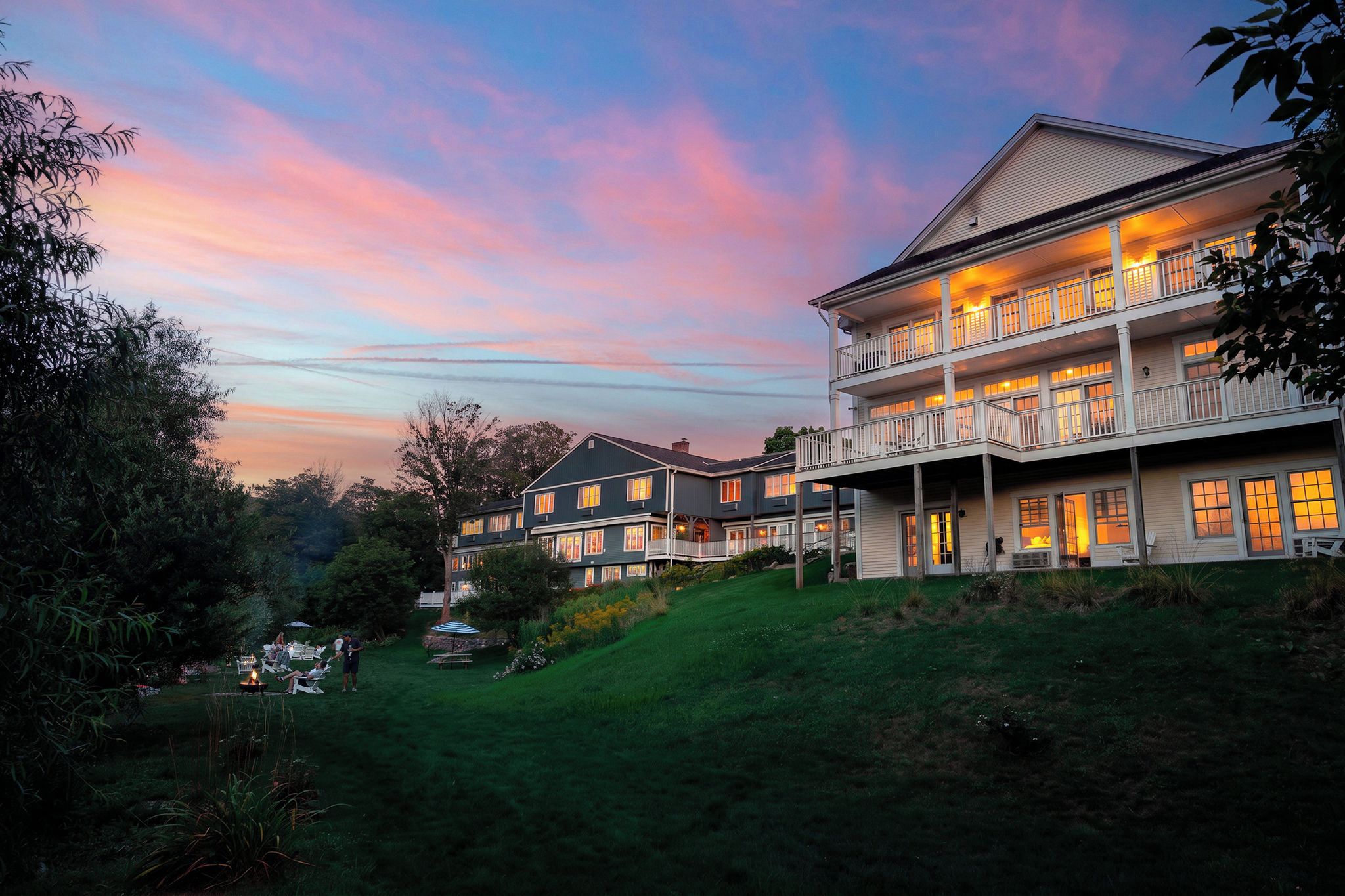 A multi-story building with a balcony, surrounded by greenery and a sunset sky.