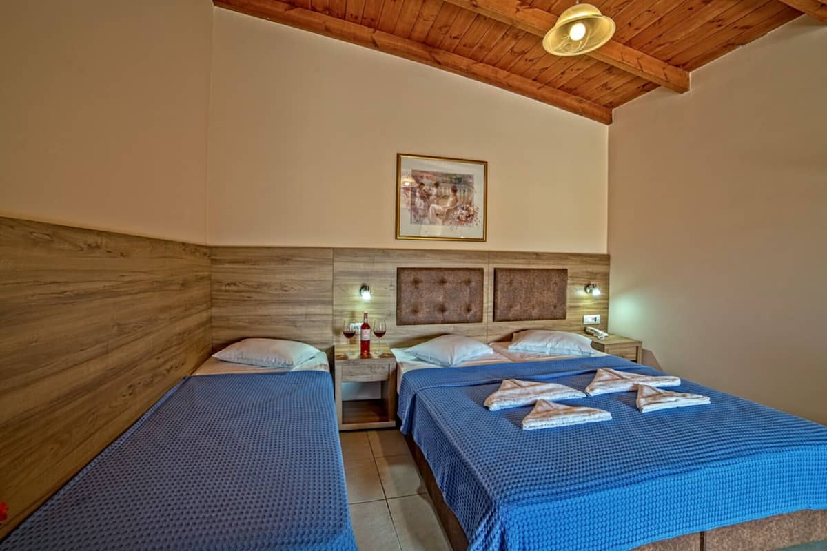 Ein Zimmer mit zwei Betten, Holzkopfteilen, einem gerahmten Bild an der Wand und einer Deckenleuchte.