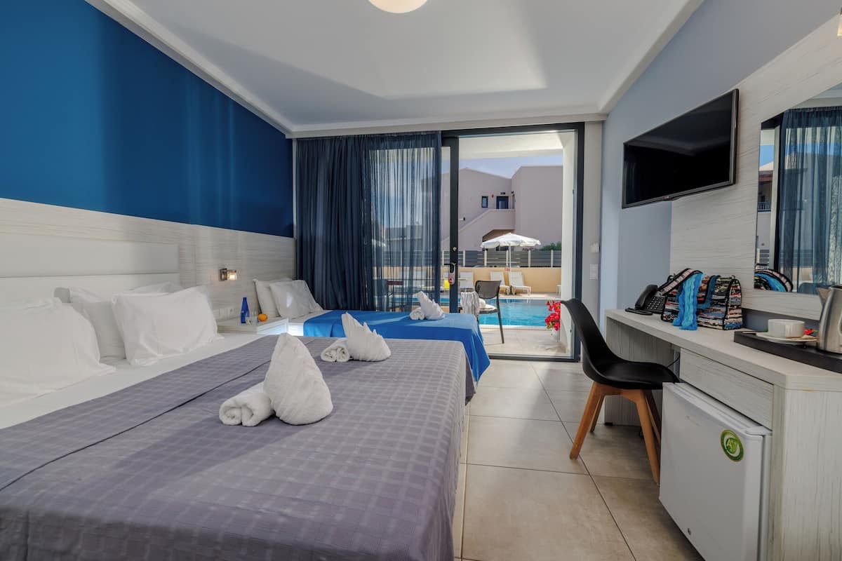 Ein Hotelzimmer mit zwei Betten, einem Schreibtisch, einem Fernseher und Blick auf den Pool.