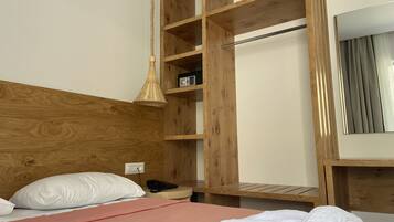 A hotel room with a wooden headboard, a bed with pink bedding, a bedside table with a phone, and a wardrobe with a mirror.