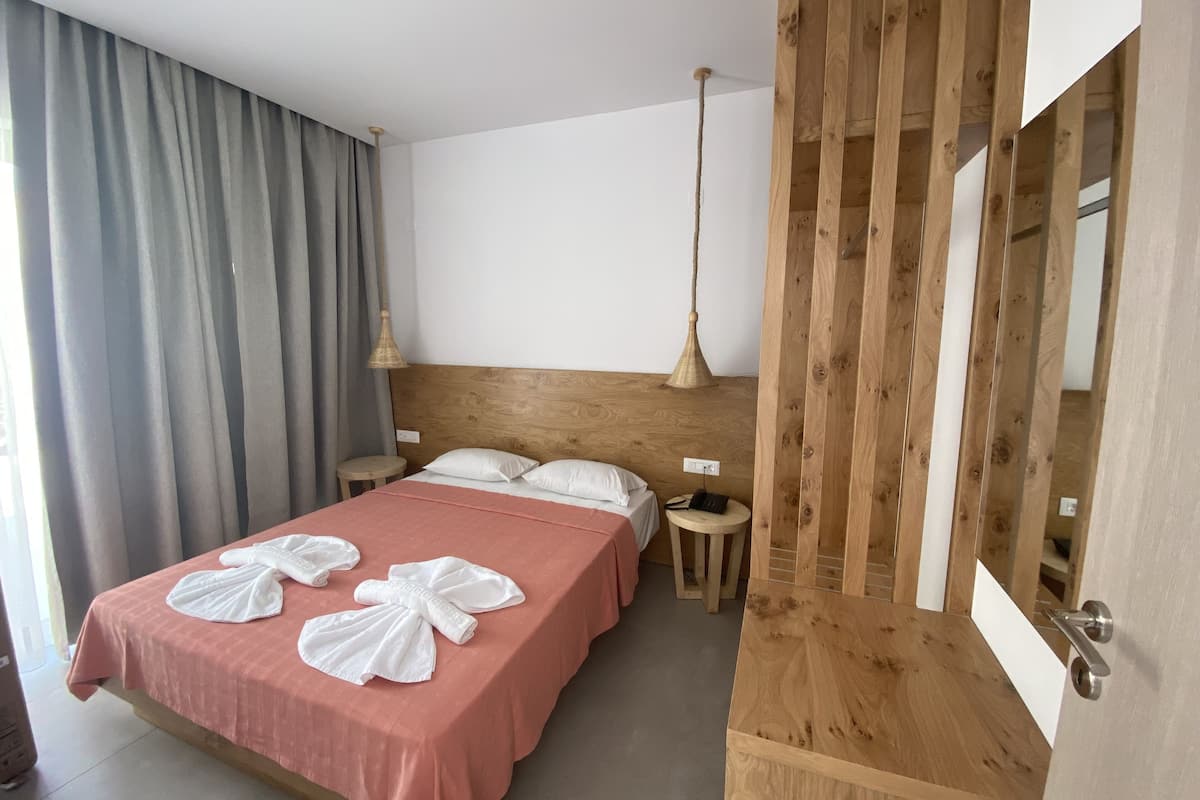 Ein Hotelzimmer mit einem hölzernen Kopfteil, einem Bett mit rosa Bettwäsche, zwei Nachttischen, einer Pendelleuchte und einem großen Fenster mit Vorhängen.