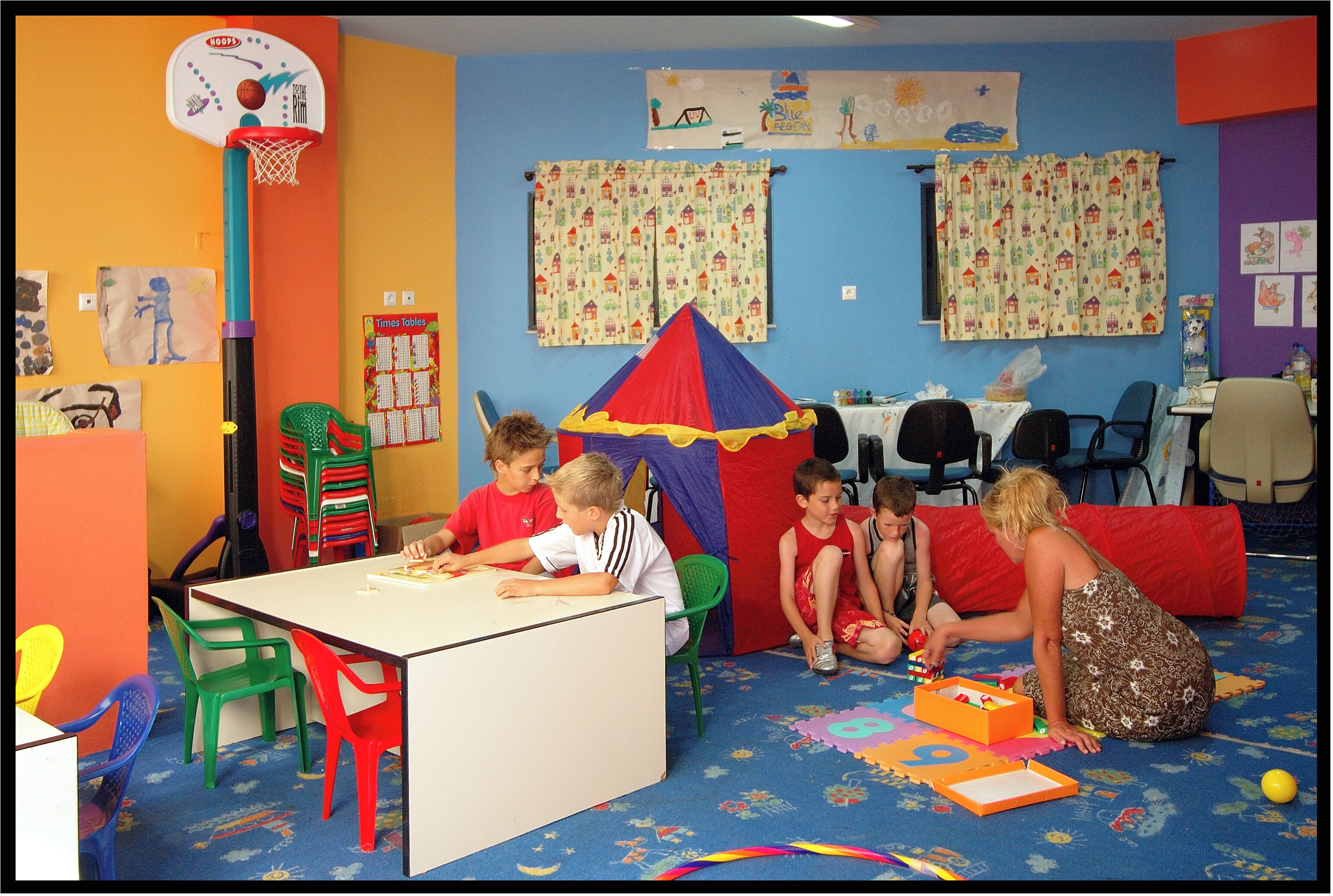 A colorful playroom with a basketball hoop, a table, chairs, and a small tent.