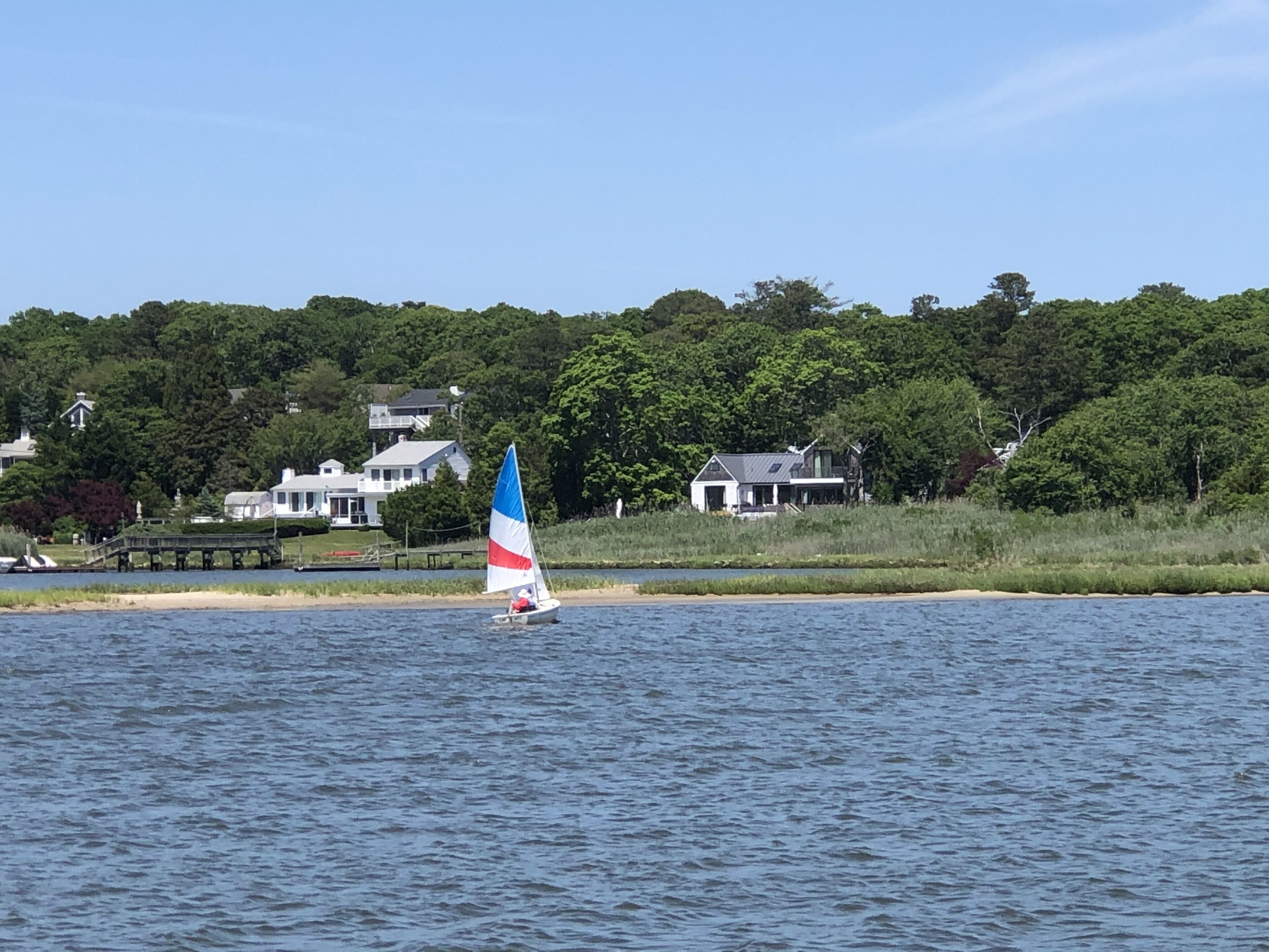 A sailboat on a calm body of water with a forested shoreline in the background.