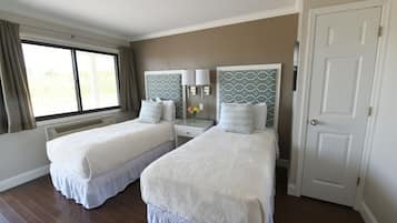 Une chambre d’hôtel avec deux lits, une fenêtre avec des rideaux, une porte blanche et une lampe fixée au mur.