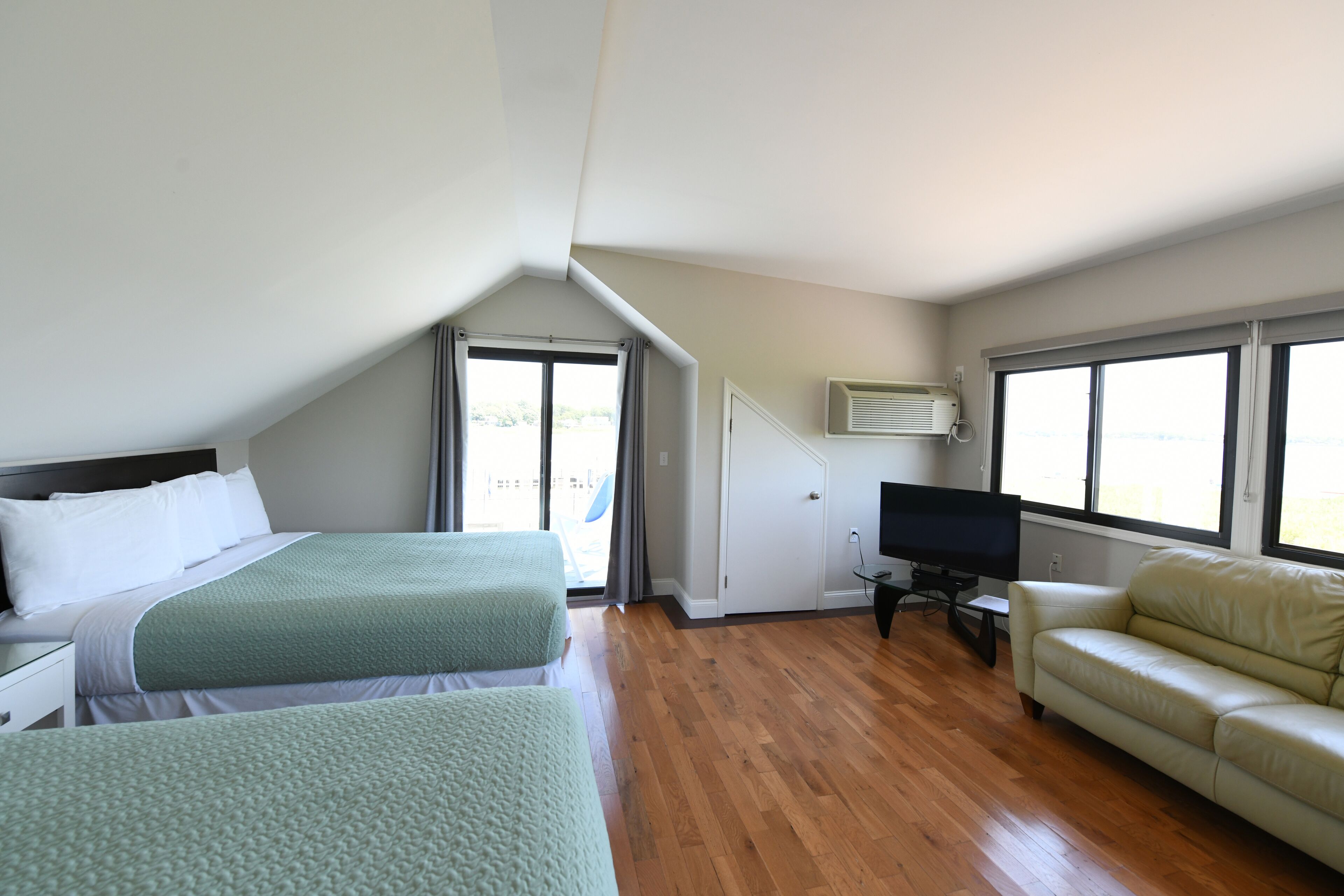 A hotel room with two beds, a TV, a sofa, and large windows.