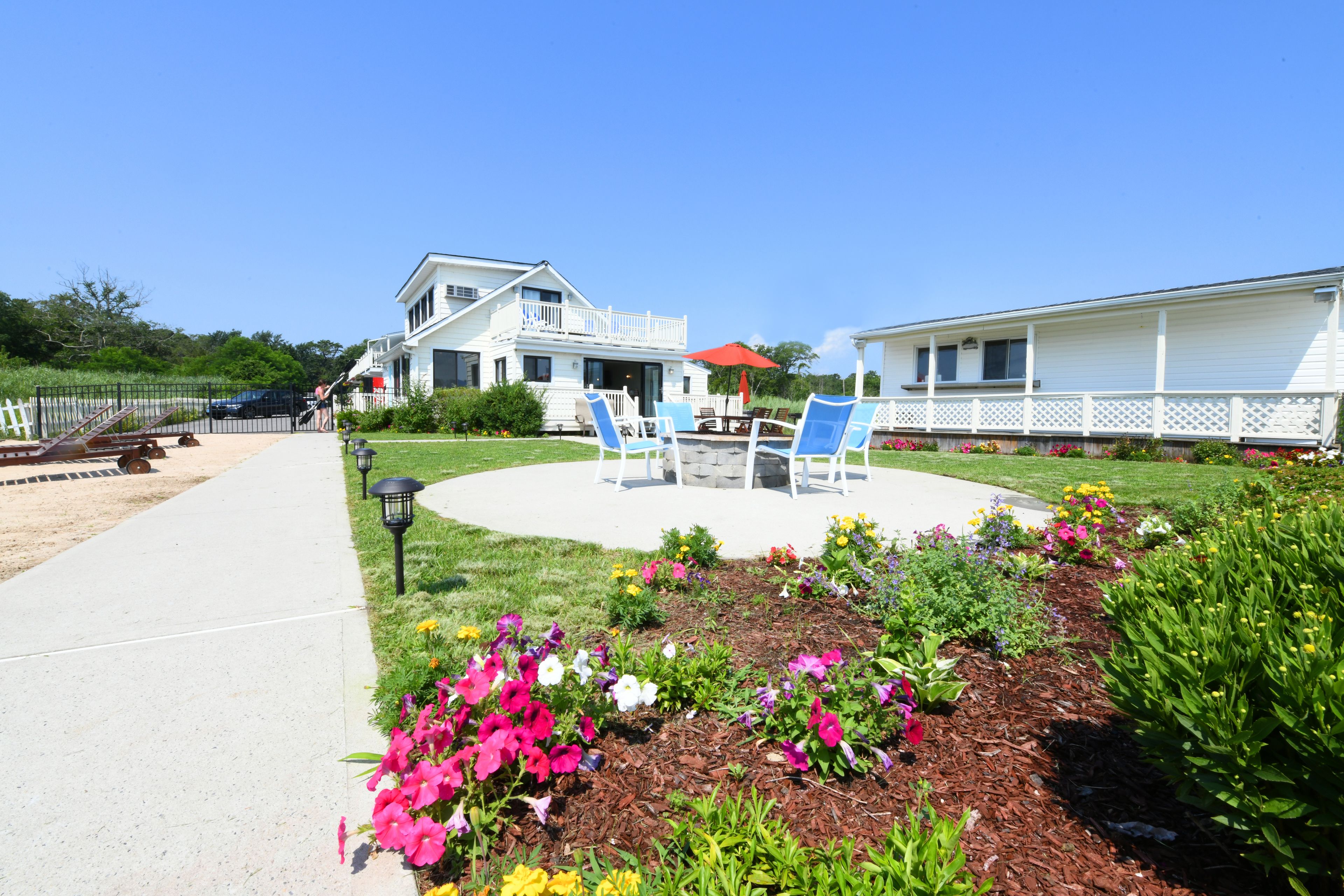 A house with a patio area featuring two blue lawn chairs and a red umbrella.