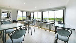A spacious dining area with large windows offering a view of the outdoors. There are multiple tables and chairs arranged for dining. - Bayview Resort (Hampton Bays)