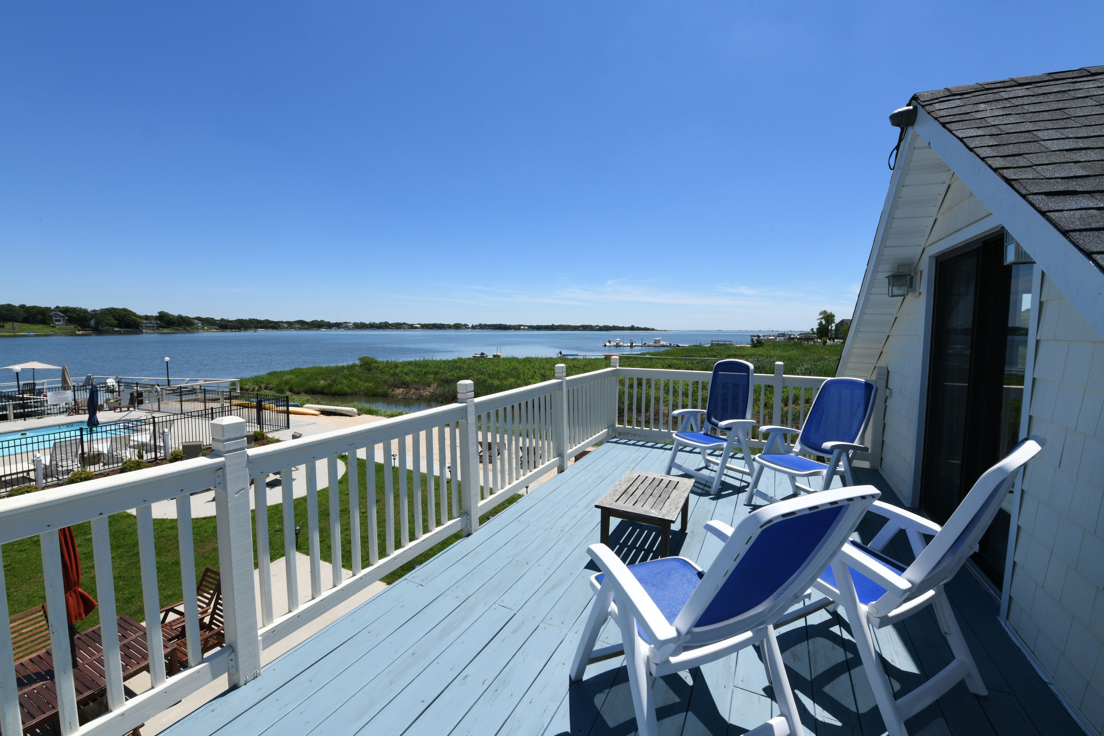 A deck with white railings, blue chairs, and a pool.