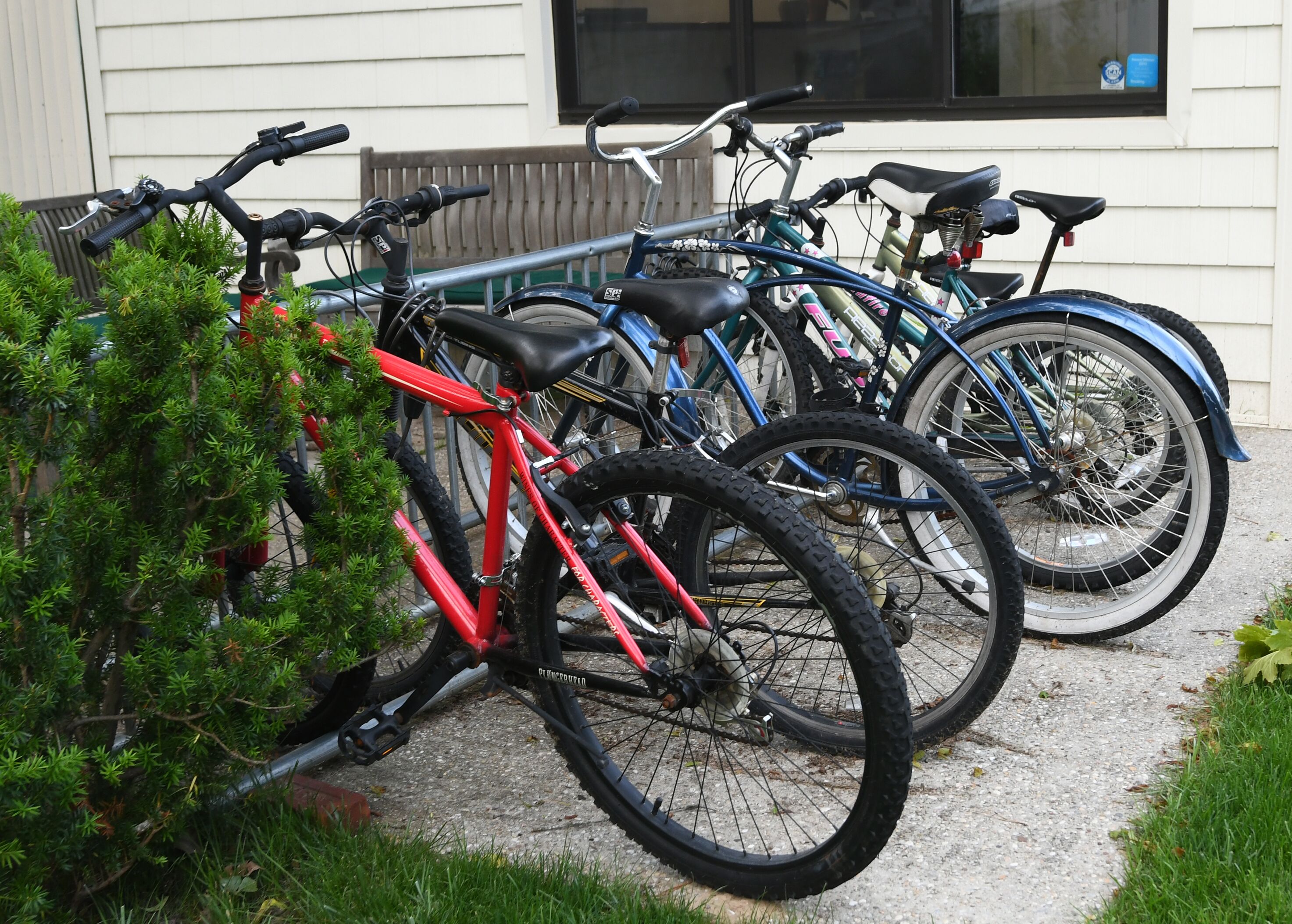 En rad cyklar står parkerade utanför en byggnad, och i bakgrunden syns ett fönster och en dörr.