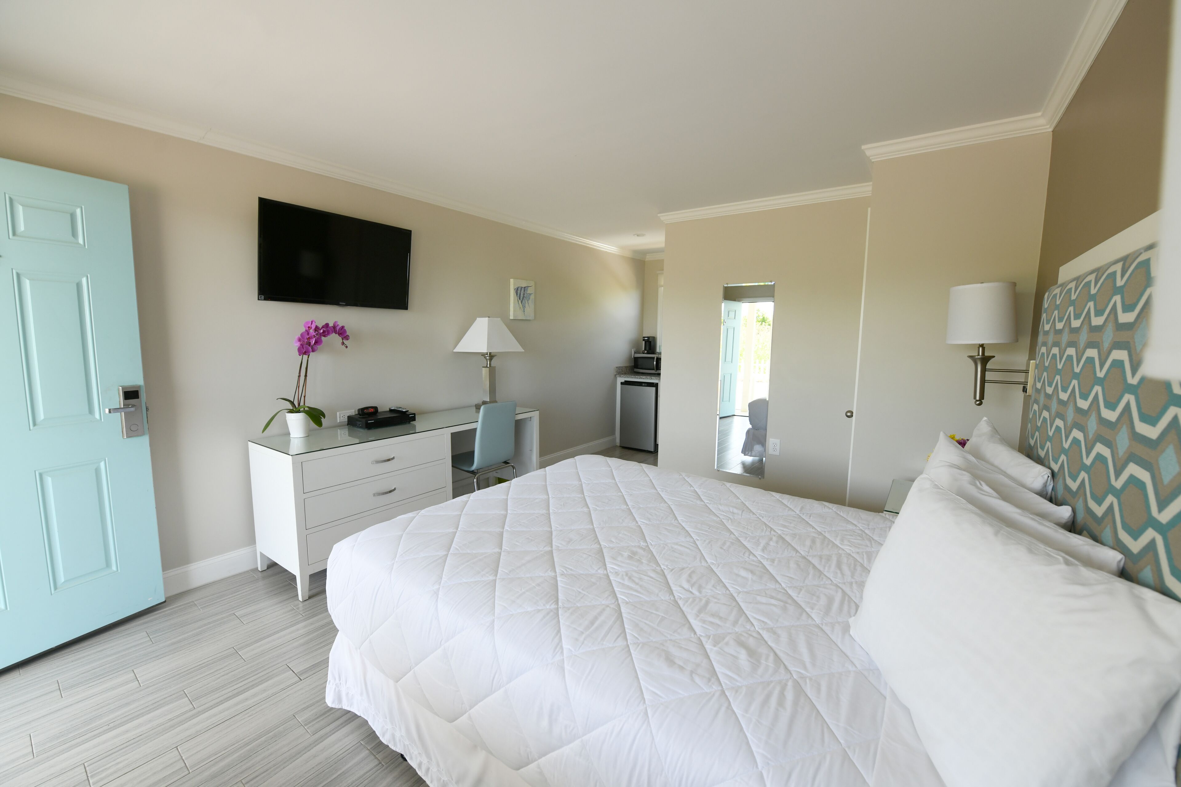 Une chambre à coucher avec un grand lit, un bureau, une chaise, une télévision et une porte.