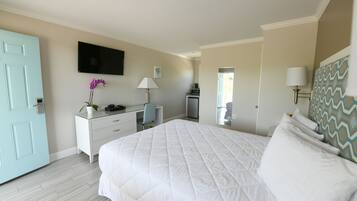 A bedroom with a large bed, a desk, a chair, a TV, and a door.