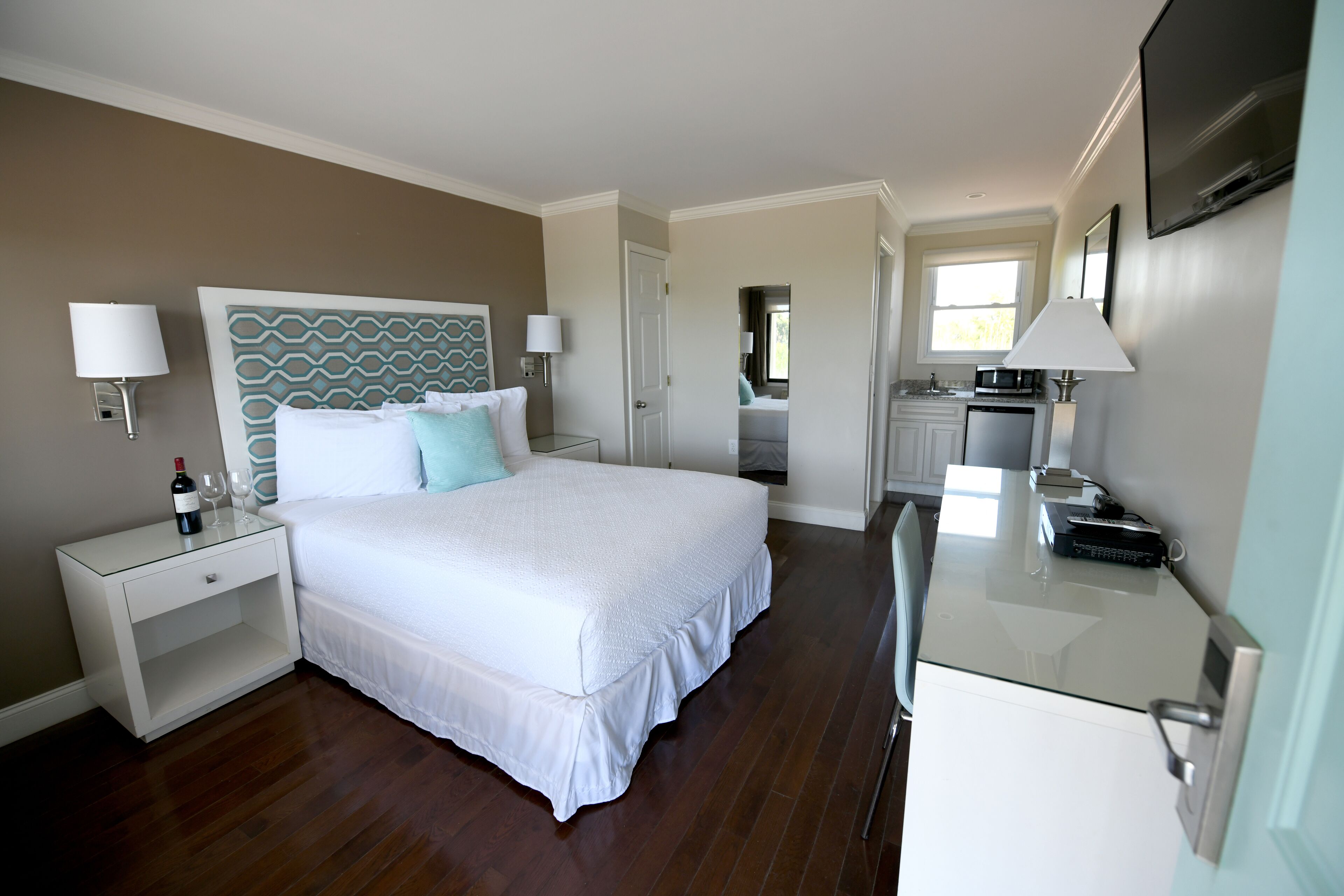 A hotel room with a large bed, bedside lamps, a small desk with a chair, and a TV mounted on the wall.