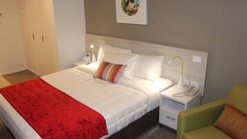 Habitación de hotel con cama, mesita de noche con lámpara, teléfono, una silla y un cuadro en la pared.