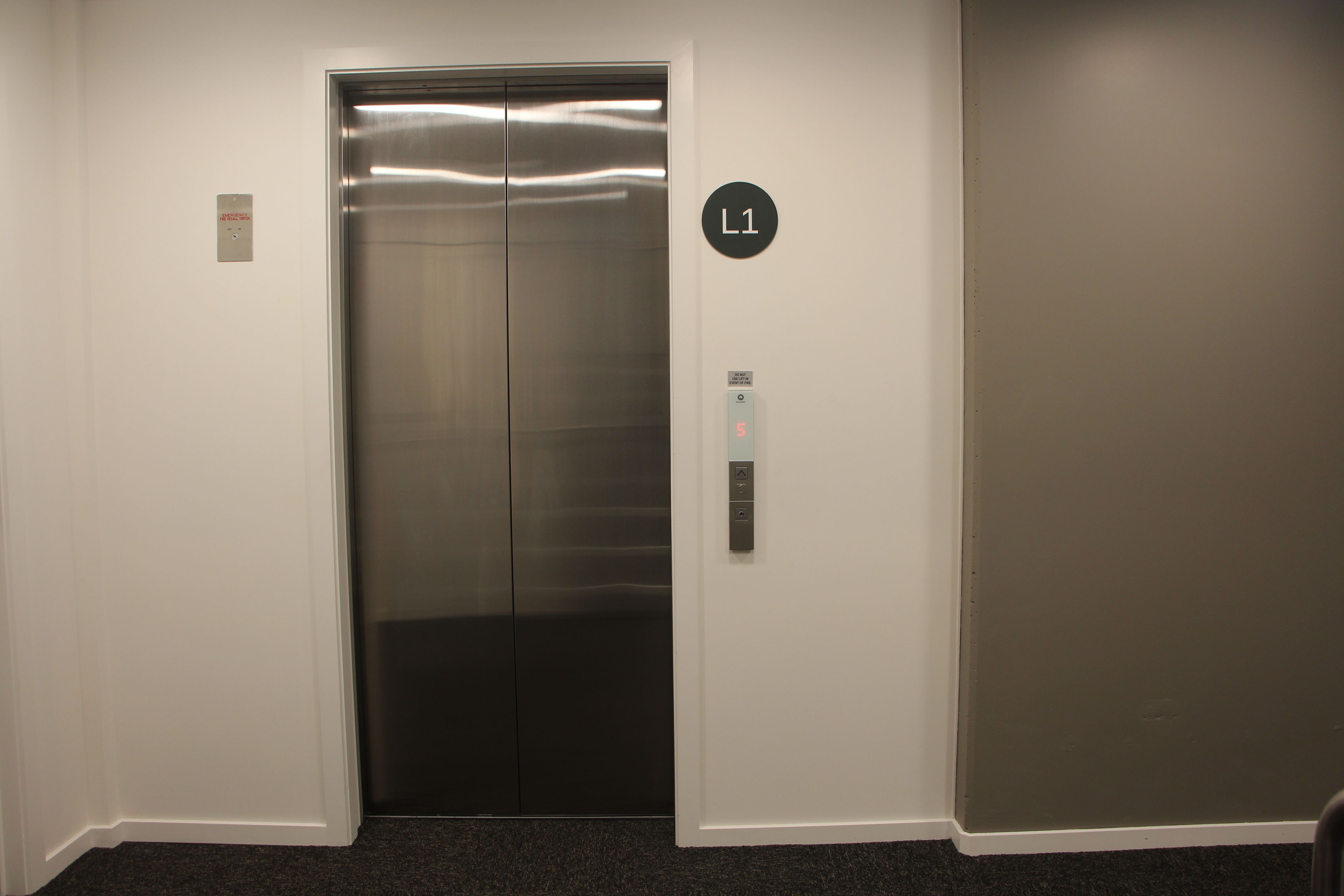 An elevator with a metallic interior, a control panel with a digital display, and a wall-mounted sign indicating the elevator's location.