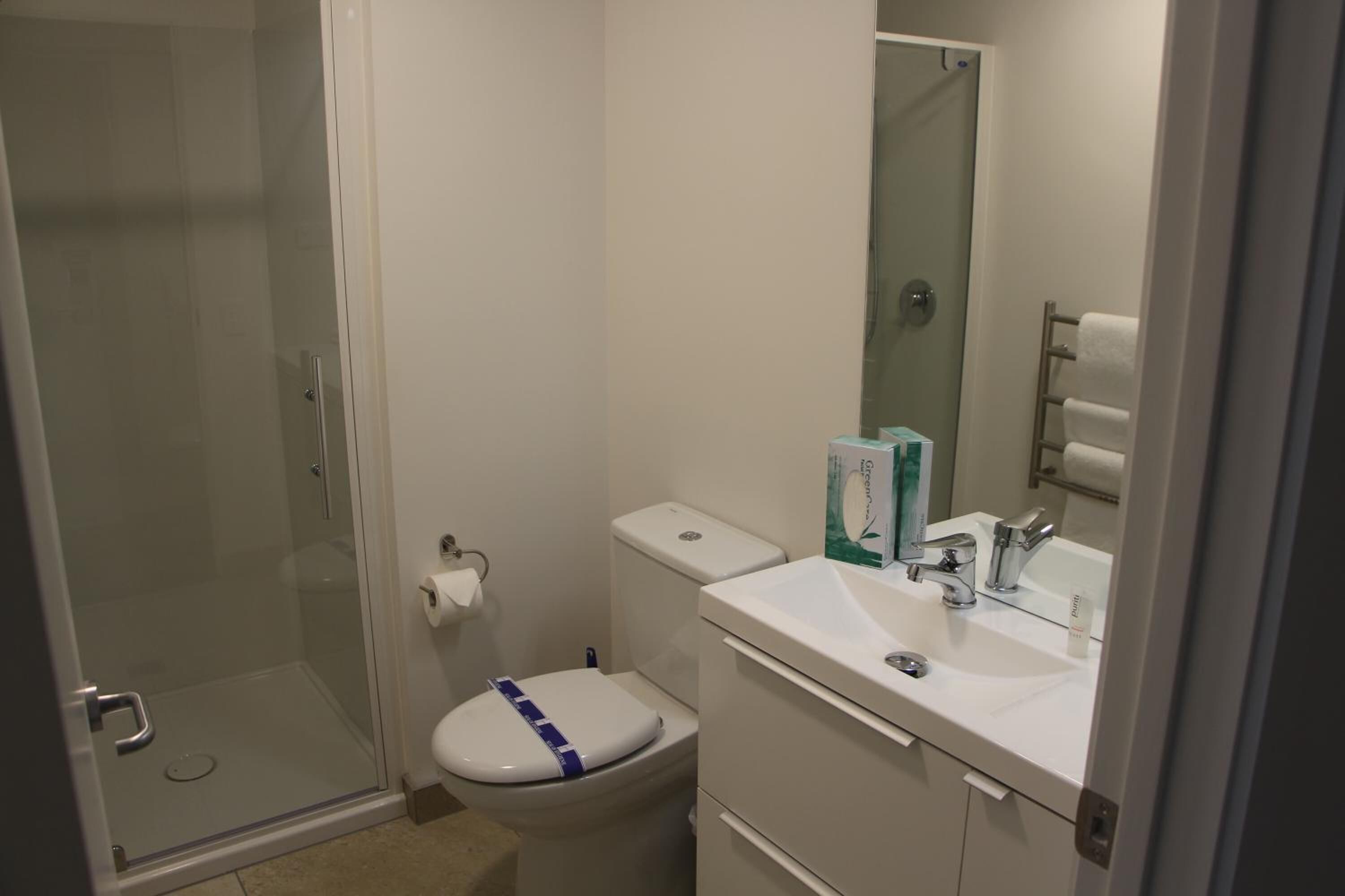 A small bathroom with a glass shower enclosure, a toilet, a sink with a mirror, and a towel rack.