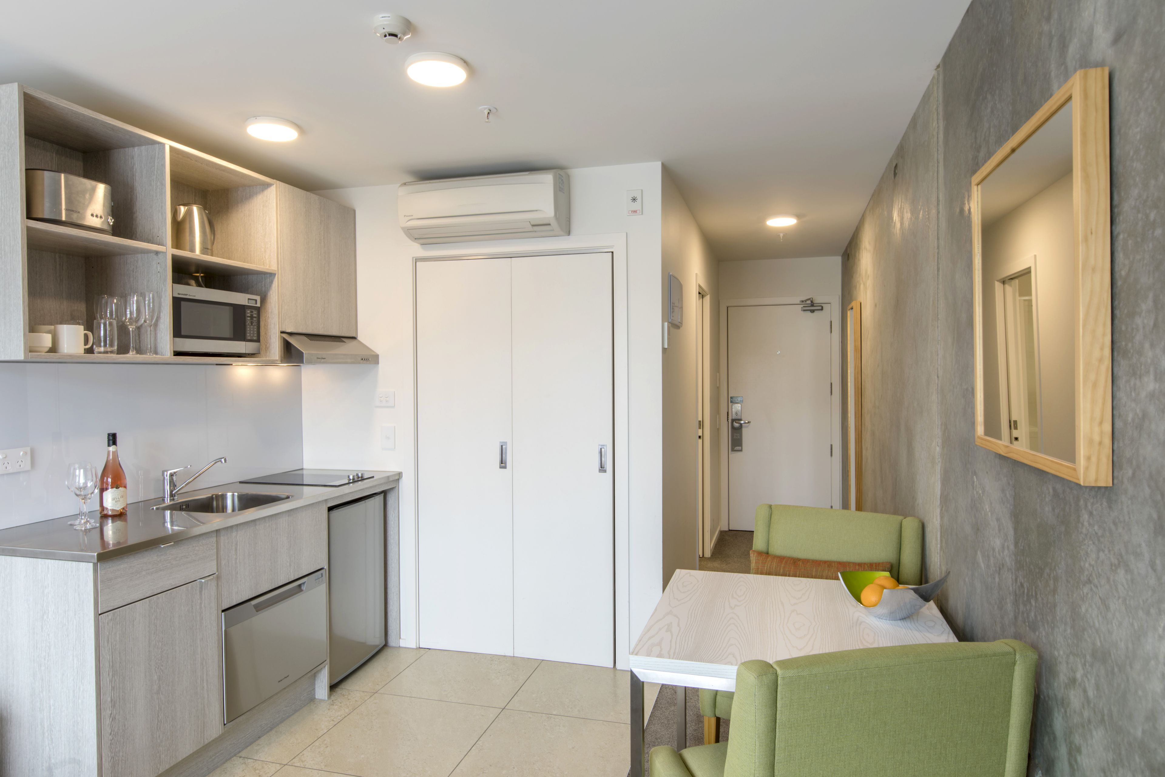 Cocina compacta con microondas, lavamanos y horno empotrado. Hay una zona de comedor con mesa y sillas.