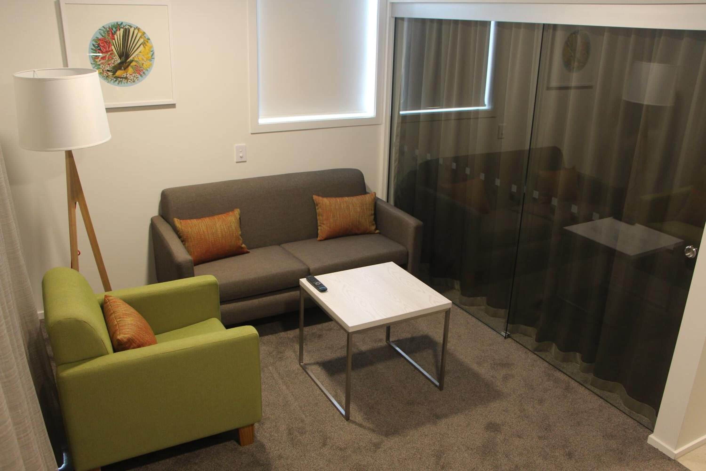 Una sala de estar con un sofá, un sillón verde, una mesita y un separador de vidrio.