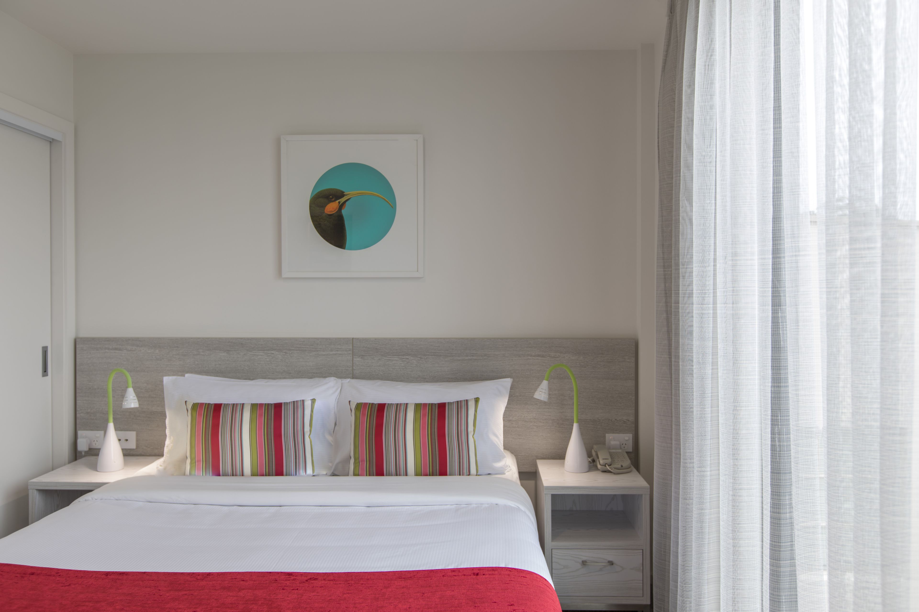 Ein modernes Hotelzimmer mit einem großen Bett, gestreiften Kissen, einem Wandbild und einem Nachttisch mit Lampe.